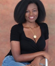 a woman with black curly hair wearing a gold necklace smiling