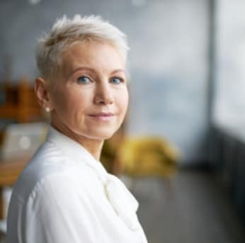 woman with pixie cut hair with blue eyes wearing a white top smiling